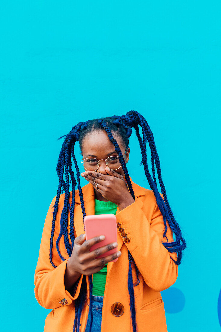 Italy, Milan, Woman with braids using smart phone against blue wall