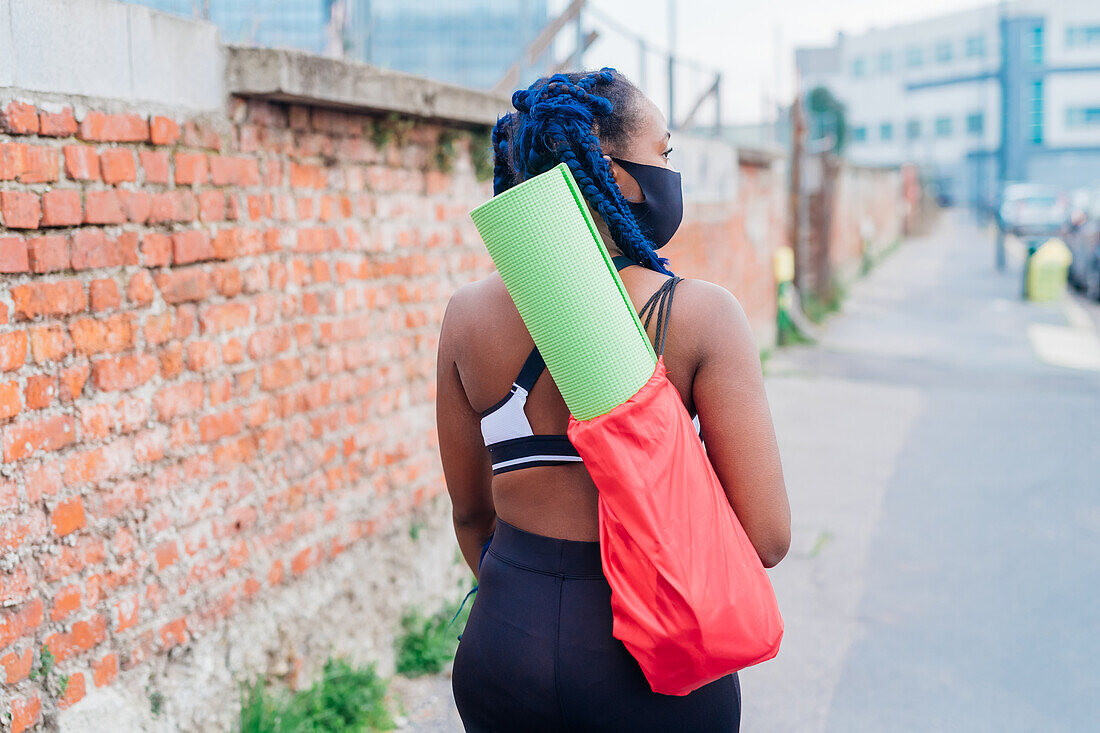 Italy, Milan, Rear view of woman carrying exercise mat in city