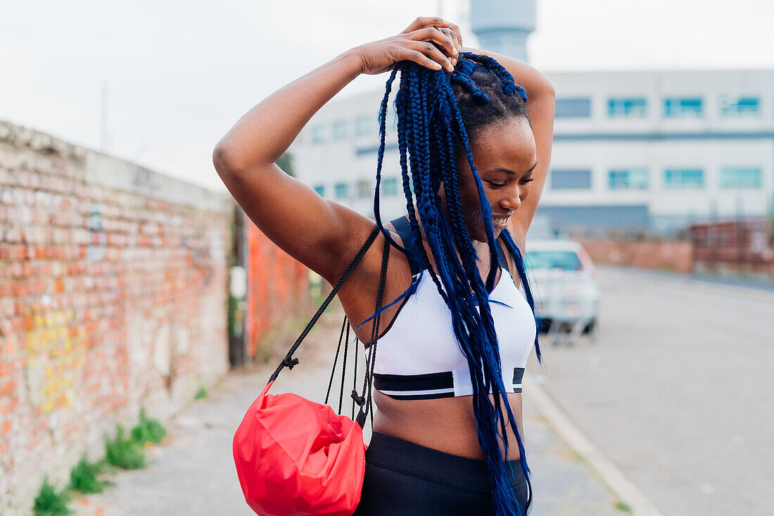 Italy, Milan, Woman in sports clothing doing her long braided hair in city