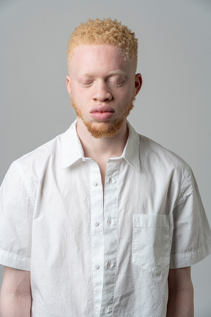 Studio portrait of albino man in white shirt with eyes closed