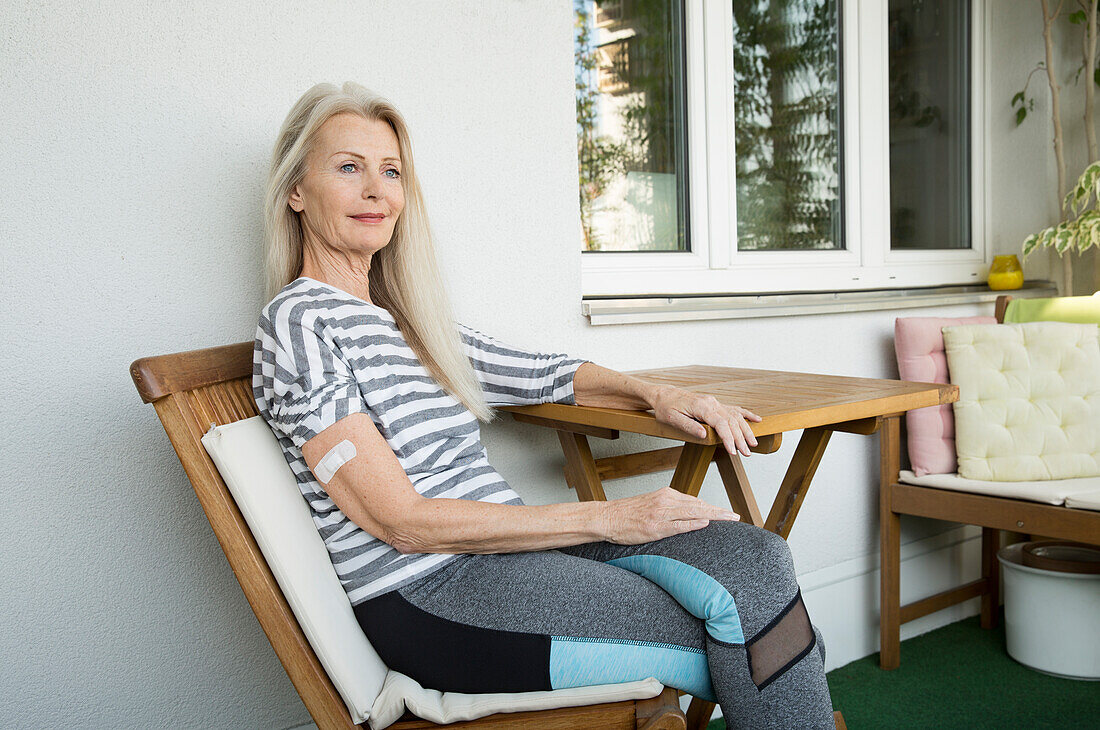 Austria, Vienna, Senior woman with adhesive bandage on arm sitting on porch