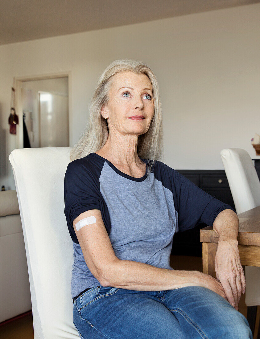 Austria, Vienna, Senior woman with adhesive bandage on arm sitting at table