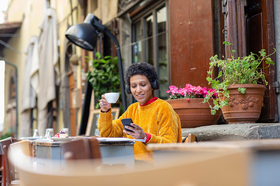 Italy, Tuscany, Pistoia, Woman sitting in outdoor cafe and using smart phone