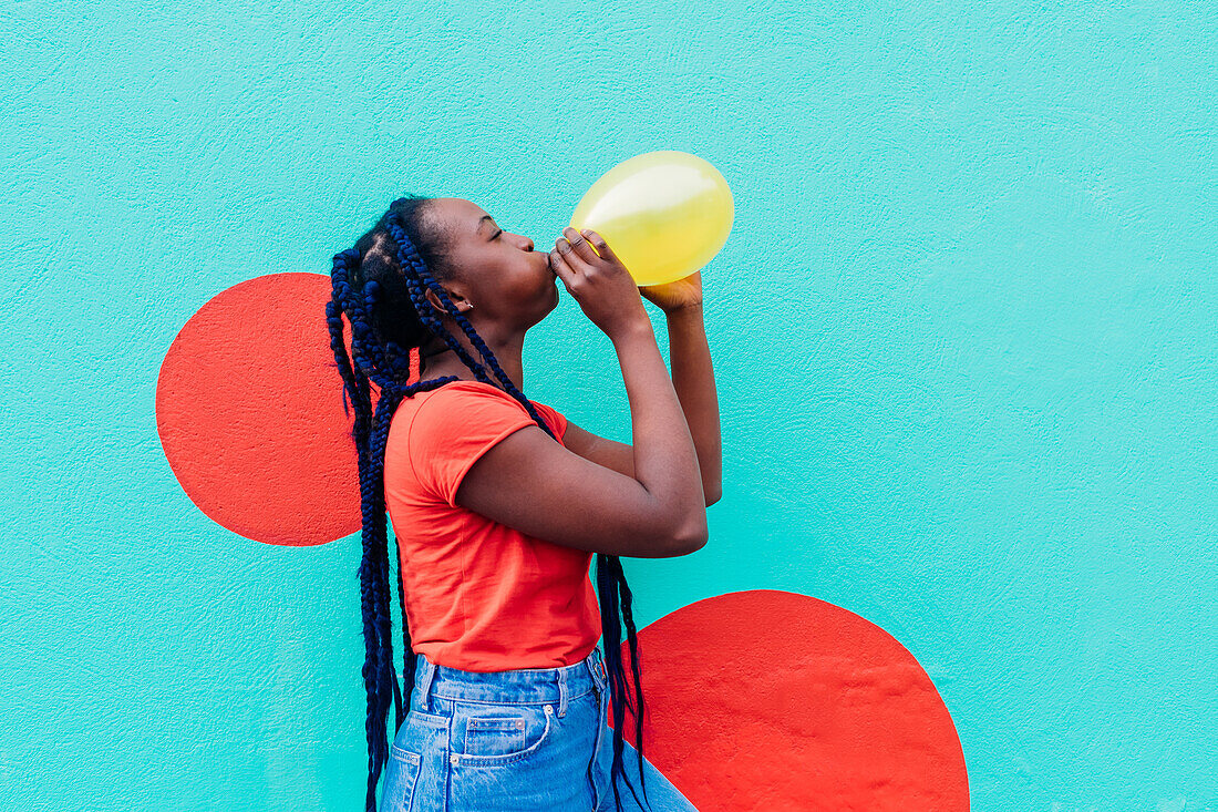 Italy, Milan, Young woman with braids blowing yellow balloon
