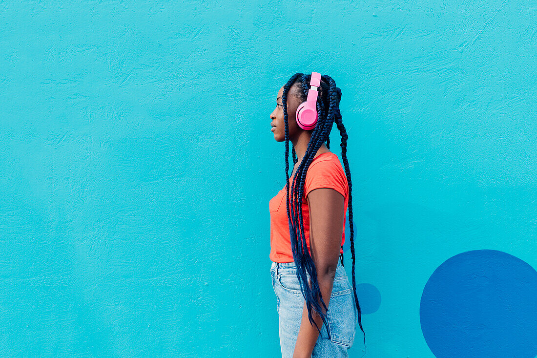 Italy, Milan, Profile of young woman with headphones in front of blue wall