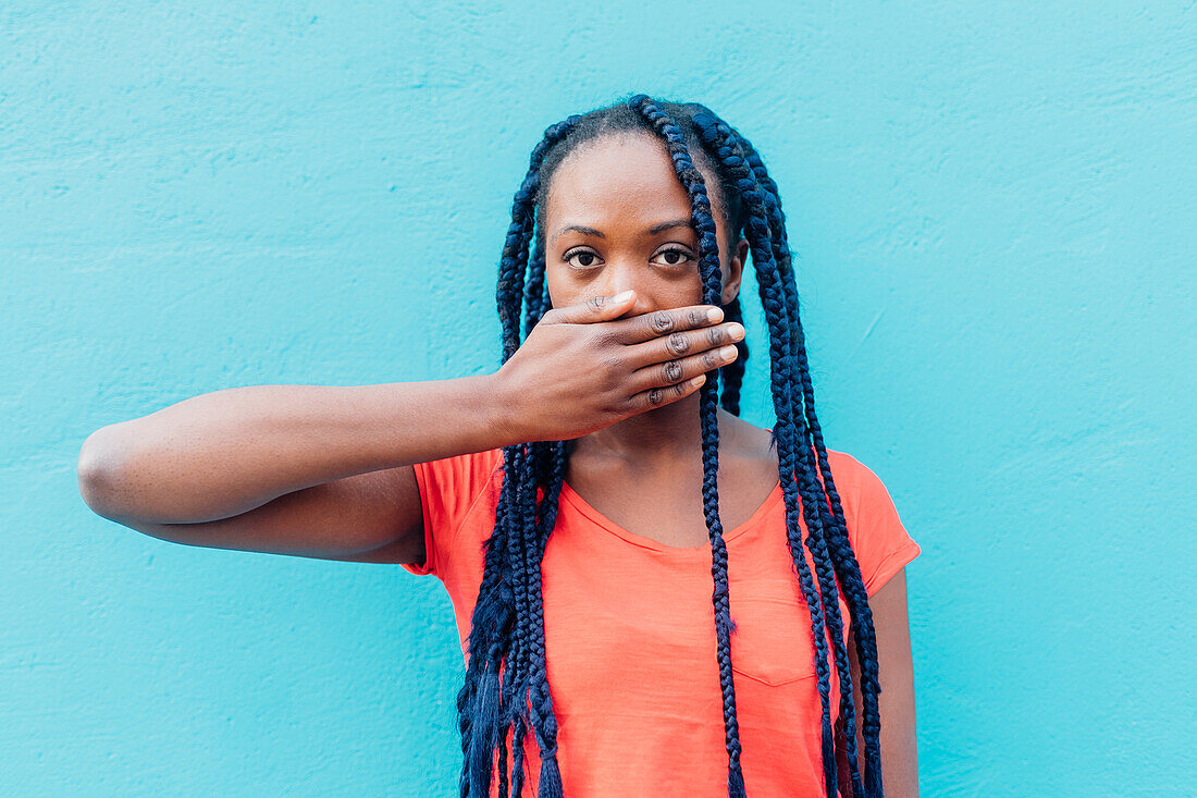 Italy, Milan, Young woman covering mouth in front of blue wall