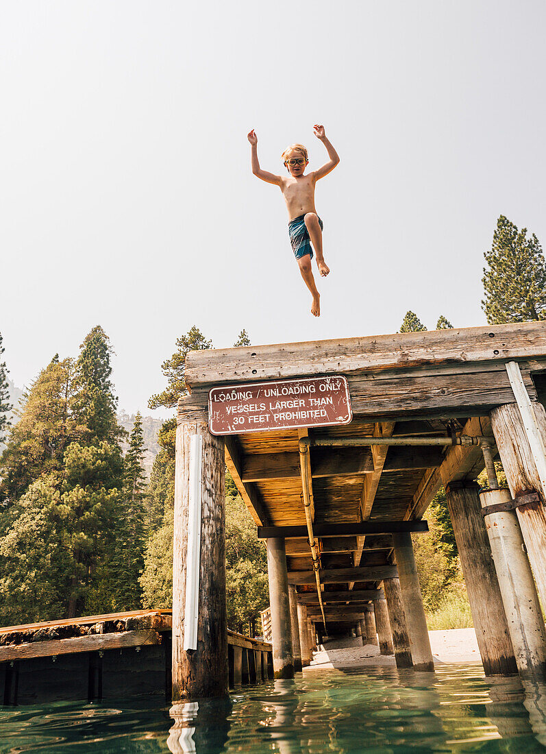 Boy (8-9) jumping from jetty into lake