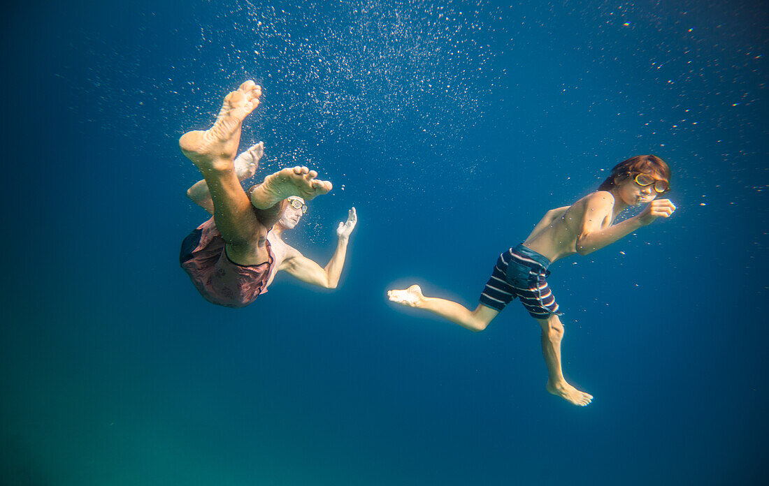 Father and son (12-13) swimming underwater