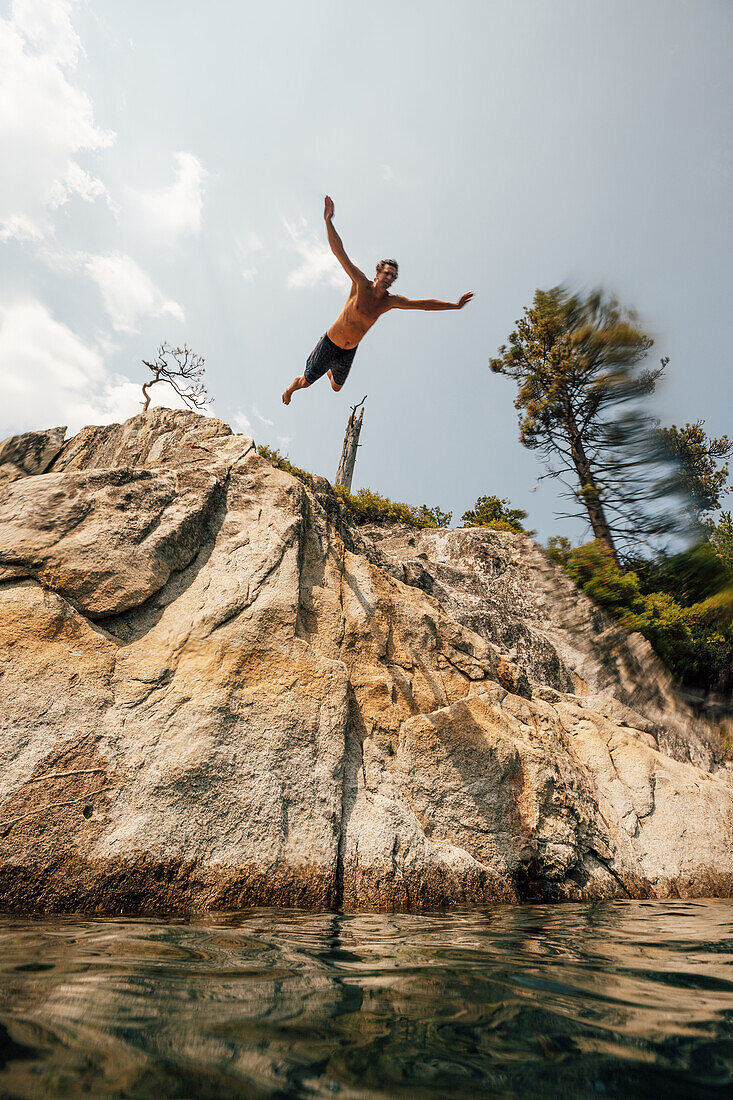 Man jumping from cliff into lake