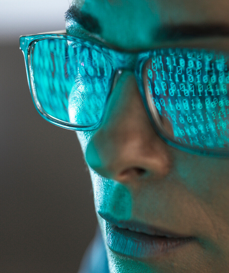Close-up of programmer with binary code reflected in eyeglasses