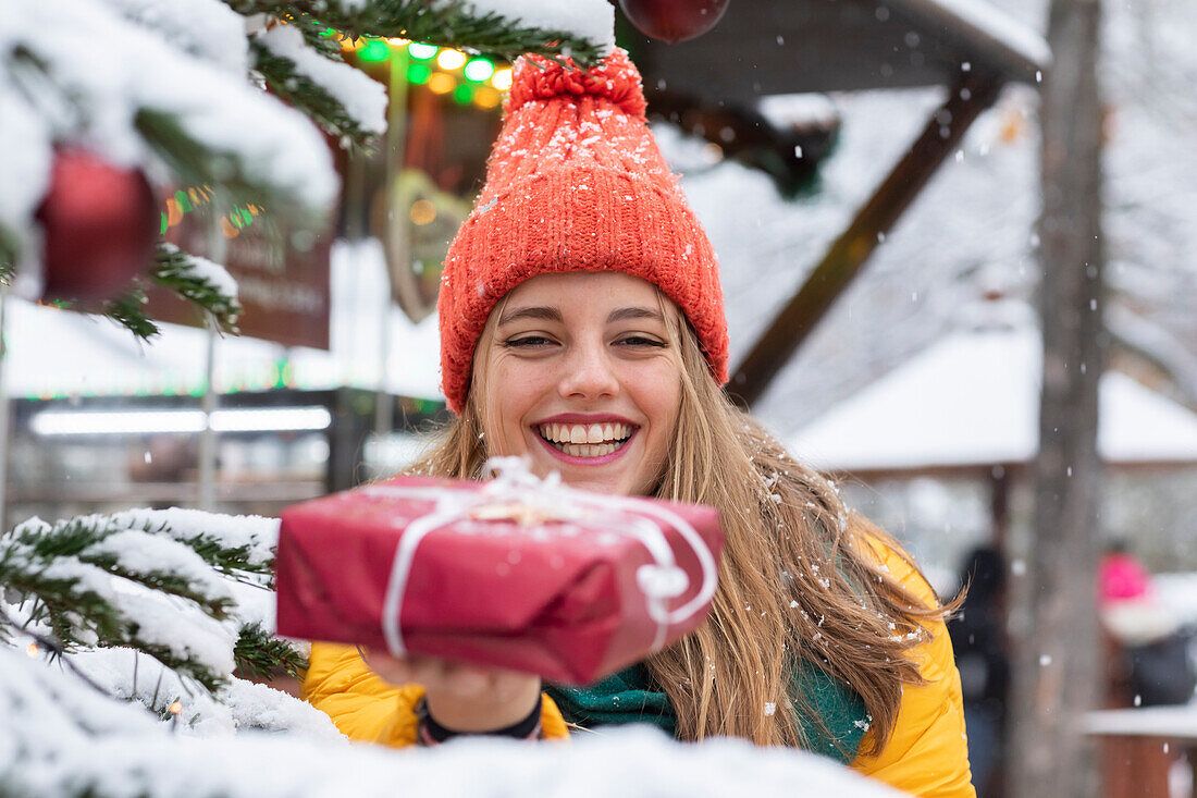 Lächelnde junge Frau mit Weihnachtsgeschenk in der Hand im Freien