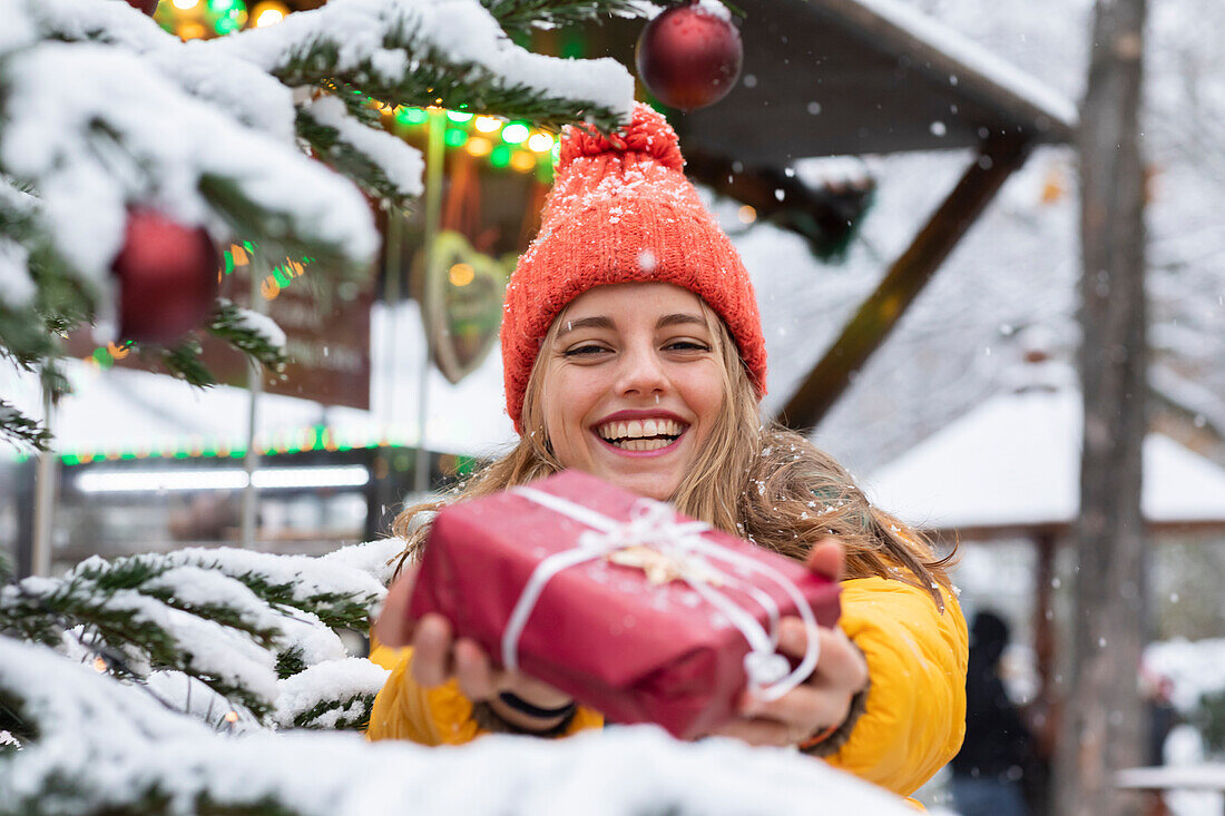 Lächelnde junge Frau mit Weihnachtsgeschenk in der Hand im Freien