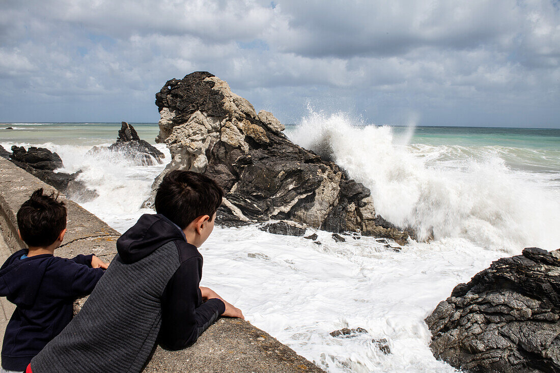 Jungen (6-7, 12-13) schauen auf Meereswellen, die gegen Felsen schlagen, Sizilien, Italien