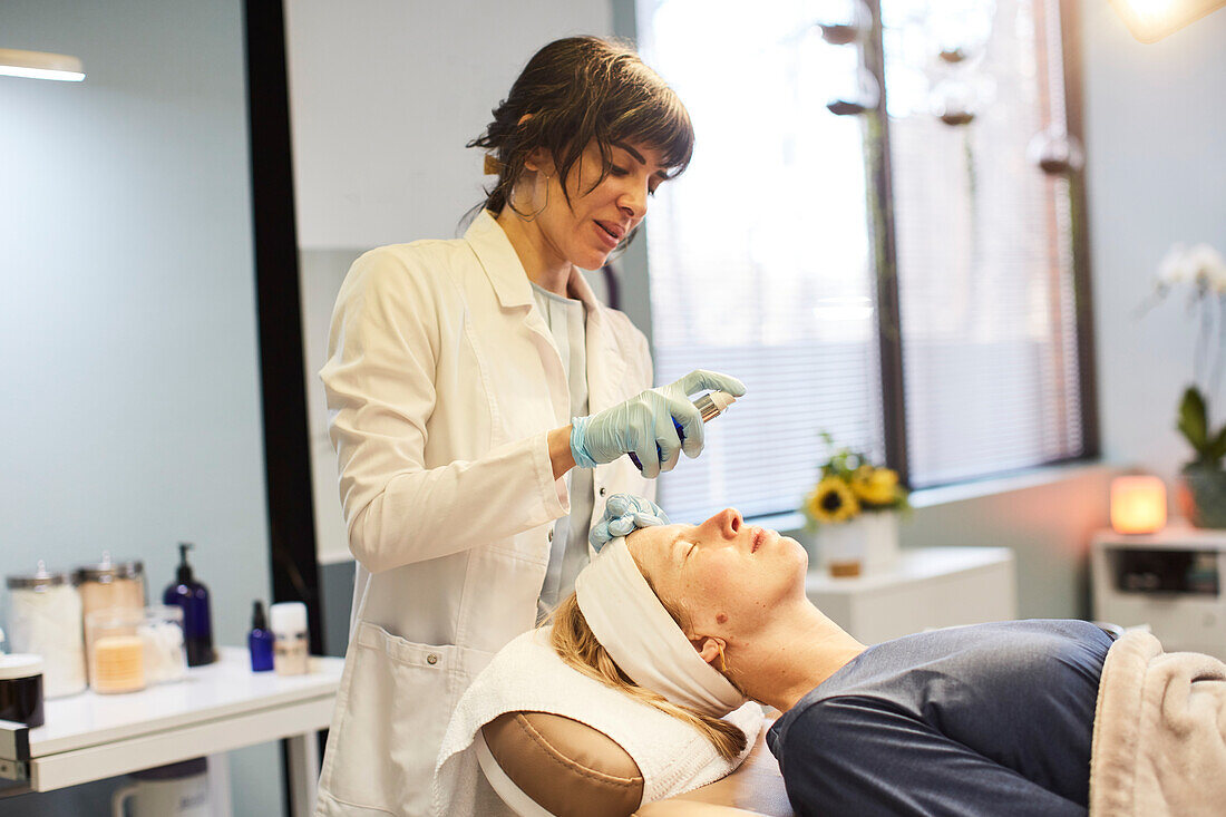 Kosmetikerin besprüht das Gesicht einer Patientin vor der Teintentfernung