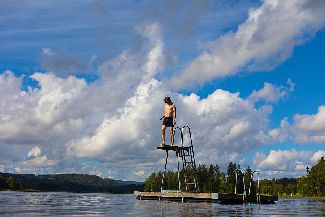 Boy (14-15) climbing diving platform on lake