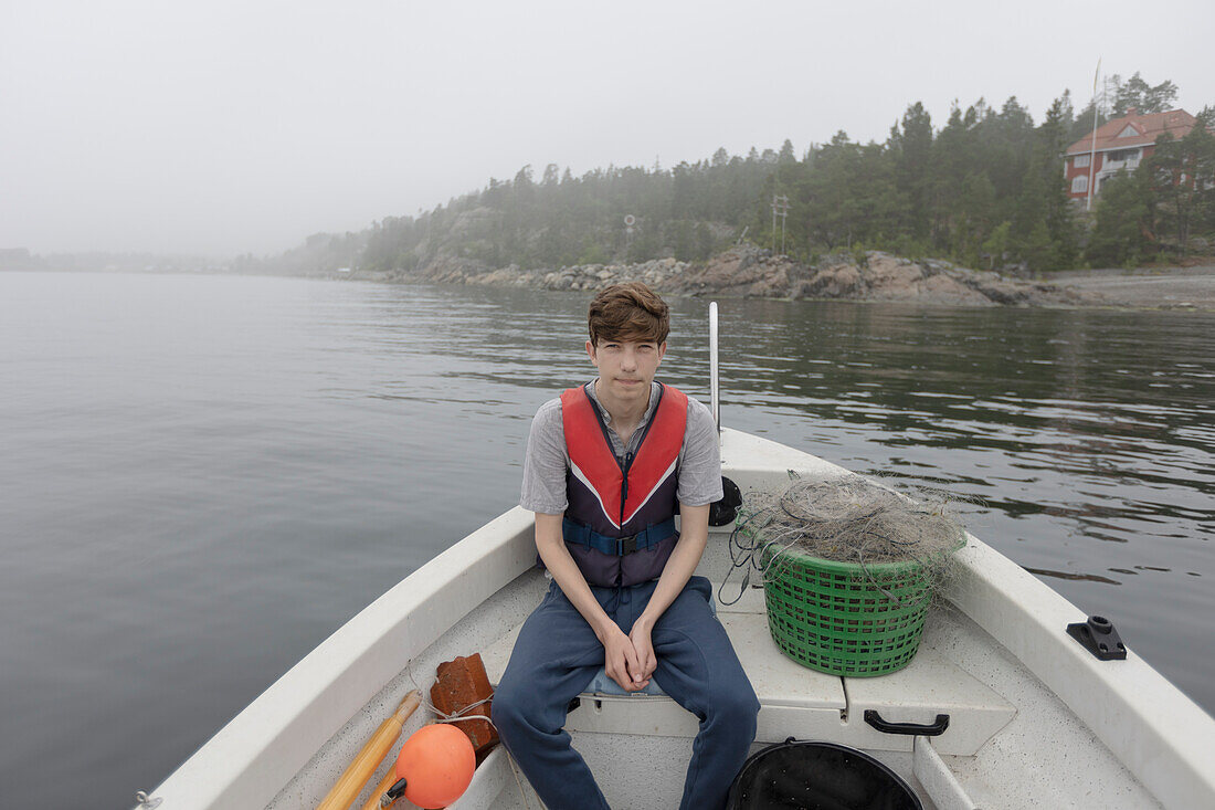 Junge (15-16) sitzt in einem Boot auf einem nebligen See