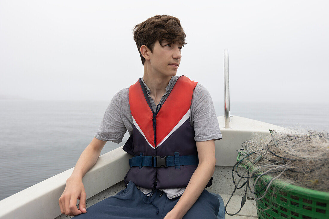 Boy (15-16) sitting in boat on foggy lake