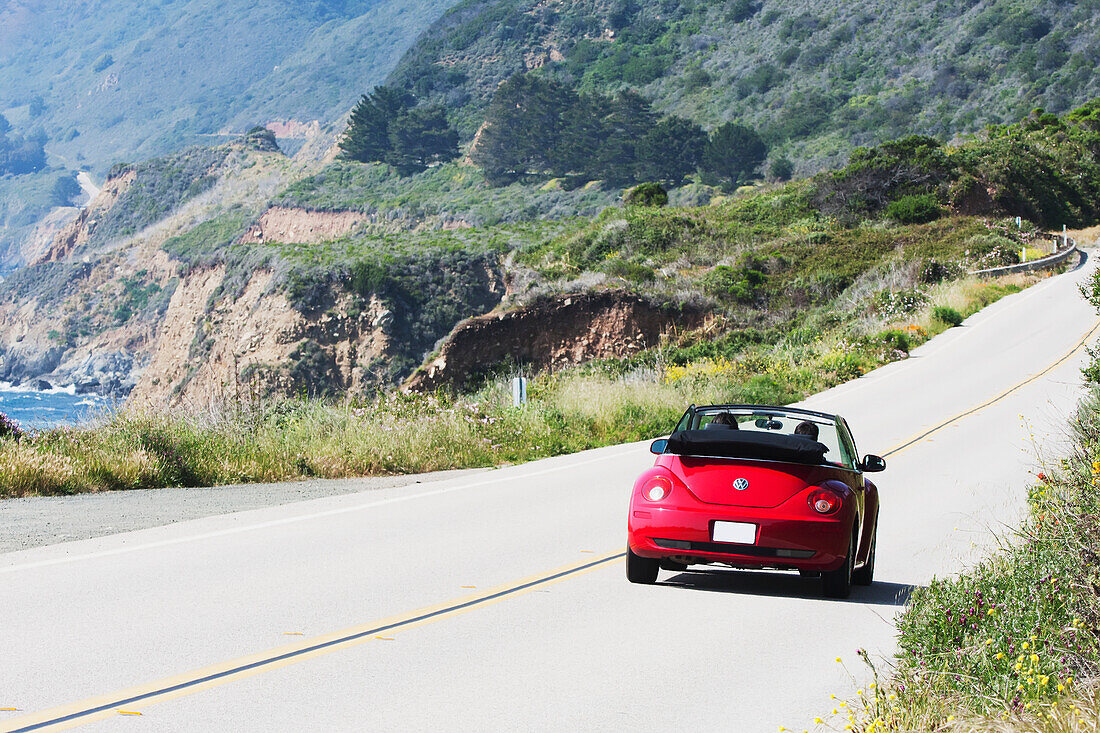 A Red Convertible Traveling Down The Highway Along The Ocean; California, United States Of America