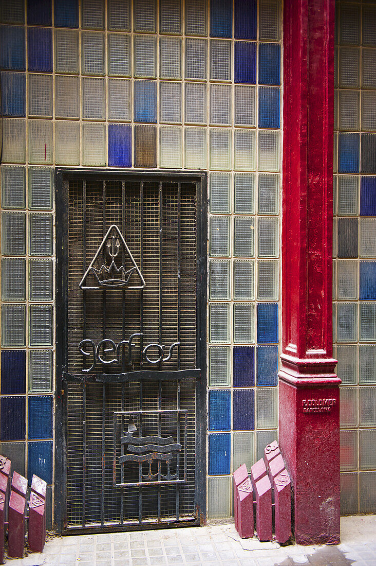 Colourful Tile On A Wall And A Red Beam Beside A Grate; Barcelona, Spain