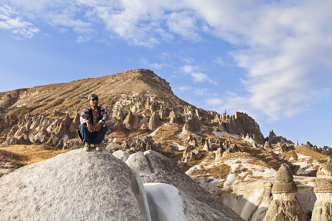 A Man Crouches On A Large Rock In A Landscape Of Fairy Chimneys; Cappadocia, Turkey