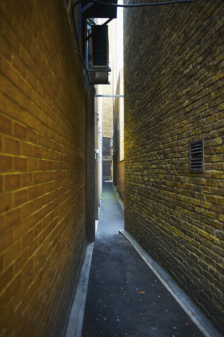 Eine schmale Gasse zwischen zwei Backsteinmauern; London, England.