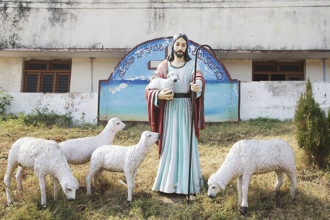 Statue von Jesus und Schafen mit einem Kreuz im Hintergrund; Visakhapatnam, Andhra Pradesh, Indien