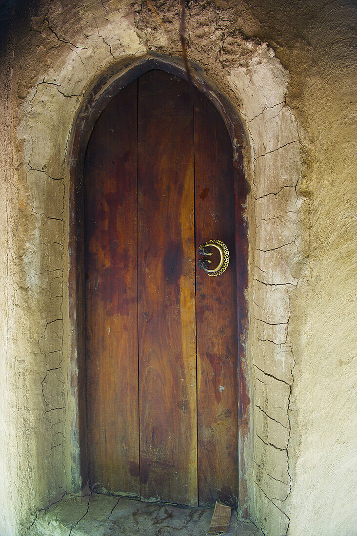Eine gewölbte Holztür mit rissiger Wand; Ulpotha, Embogama, Sri Lanka.