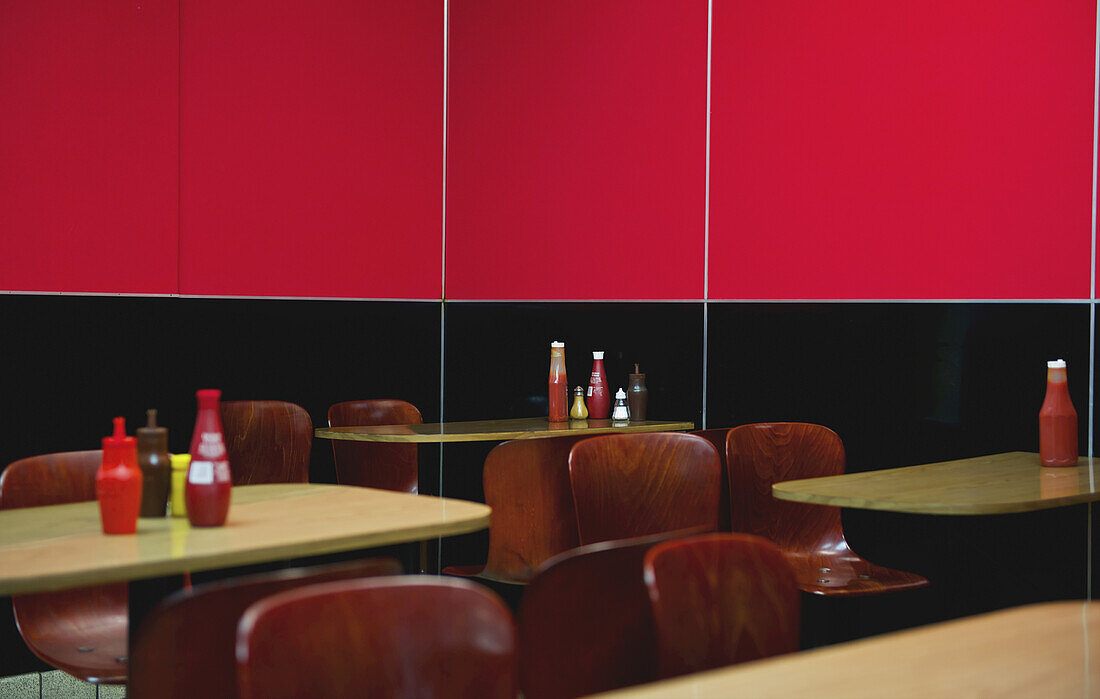 Sitzplätze in einem Restaurant mit einer halb schwarzen und halb leuchtend roten Wand; London, England.