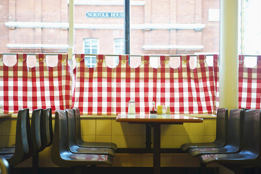 Ein Restaurant mit rot-weiß-karierten Vorhängen am Fenster und einer gelben Wand; London, England.
