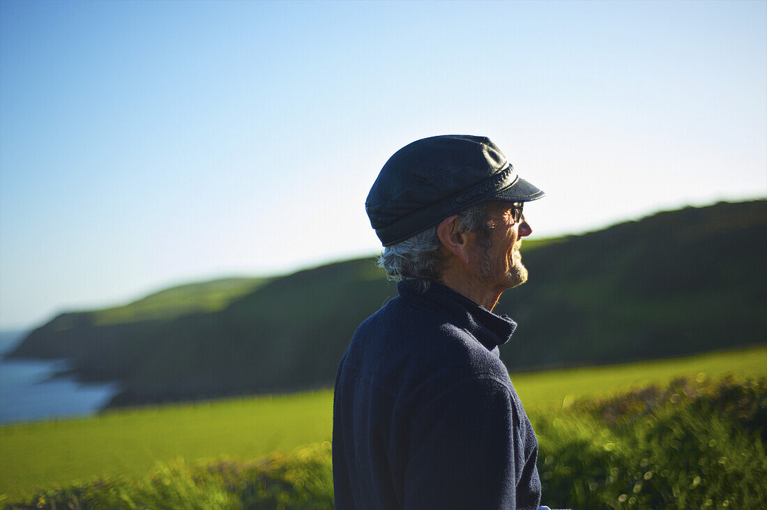 Ein Mann mit Sonnenlicht im Gesicht, der auf eine üppige Landschaft im Hintergrund blickt; Lleyn Peninsula; Wales
