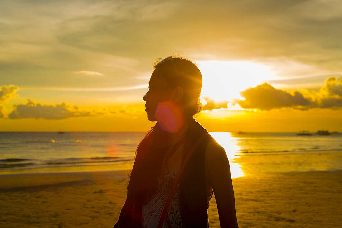 Eine Frau steht am Strand von Boracay in einem glühenden goldenen Sonnenuntergang; Panay, Philippinen