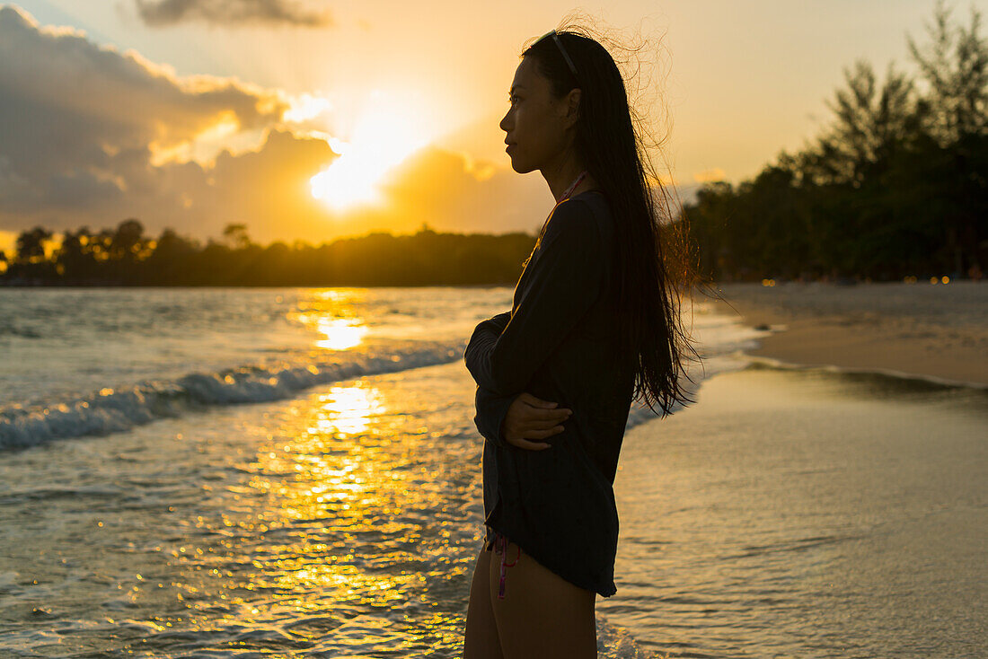 A Young Woman Stands Posing On Sokha Beach At Sunset; Sihanoukville, Cambodia