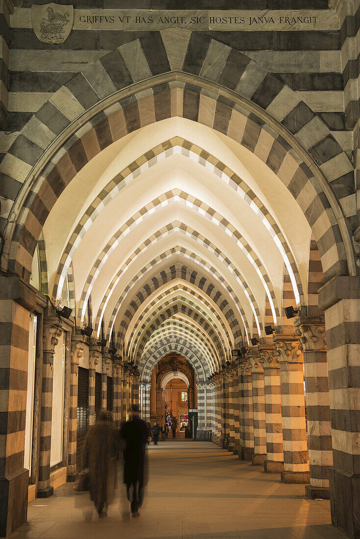 Pedestrians Walk Down An Arched Corridor With Striped Black And White Facade; Genoa, Liguria, Italy