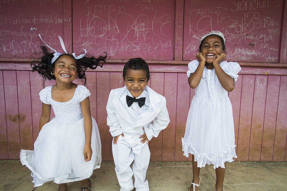 Kinder in weißer Festkleidung vor roter Wand; Hapai-Insel, Tonga