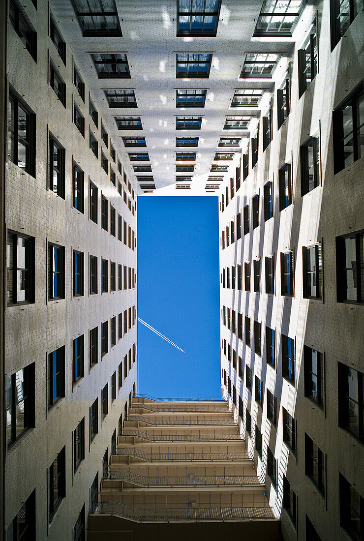 An Airplane Flying In A Blue Sky And Seen From The Ground Up The Walls Of A Residential Building; Denver, Colorado, United States Of America