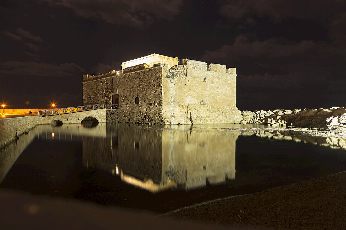 Eine alte mittelalterliche Burgruine spiegelt sich nachts im ruhigen Wasser; Paphos, Zypern