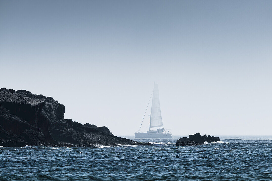 Felsen an der zerklüfteten Küstenlinie mit einem Segelboot im Nebel; Tarifa, Cadiz, Andalusien, Spanien