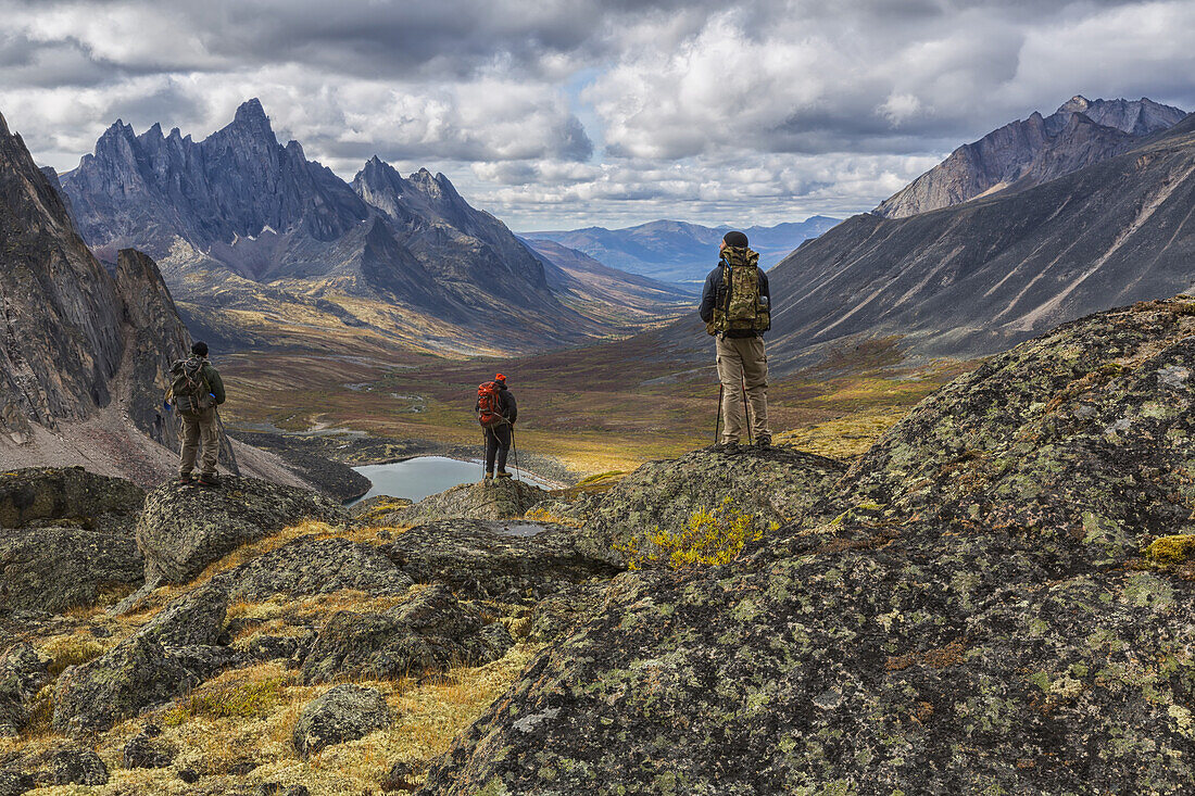 A Group Of Hikers Standing On Rocks Overlooking The Colourful Valleys In Tombstone Territorial Park In Autumn; Yukon, Canada
