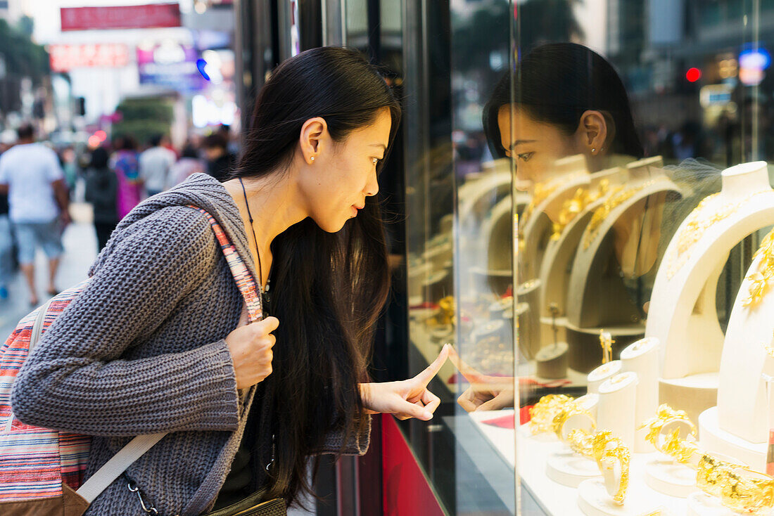 Eine junge Frau beim Schaufensterbummel in den Einzelhandelsgeschäften entlang der Straße, Kowloon; Hongkong, China.