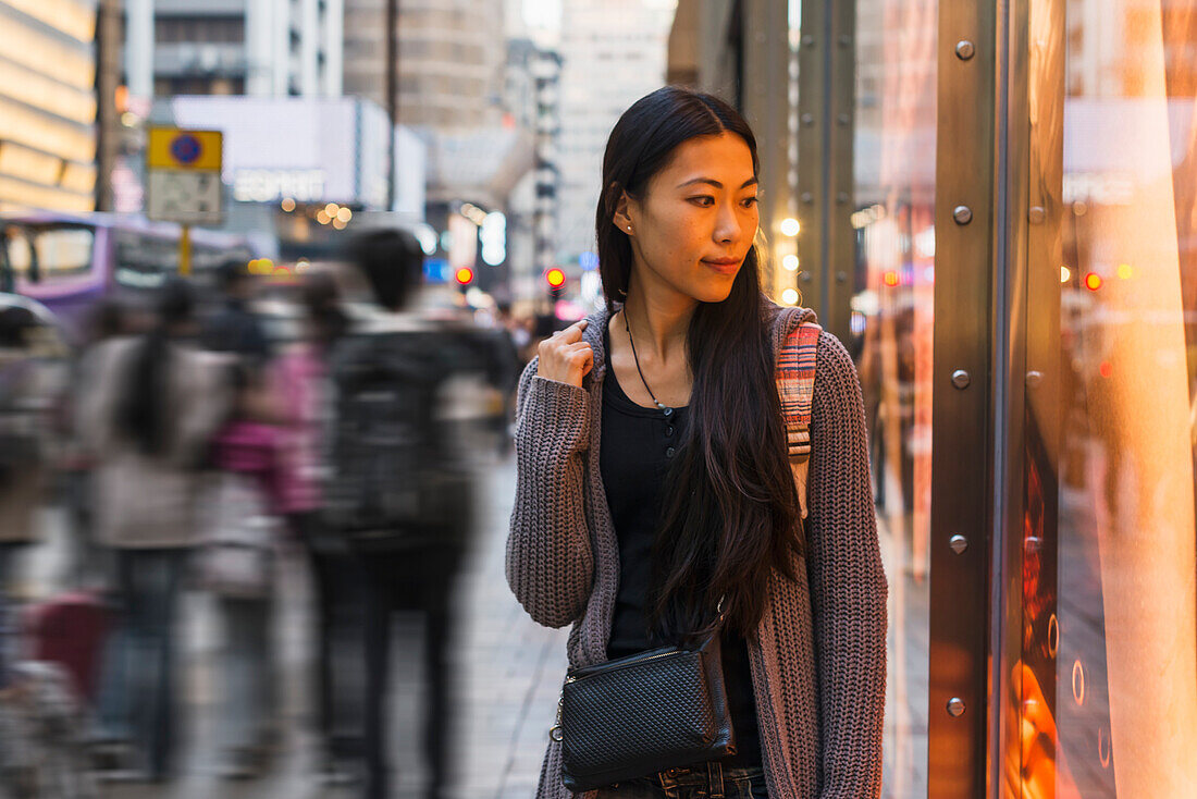 Eine junge Frau geht entlang der Straße und der Geschäfte, Kowloon; Hongkong, China.