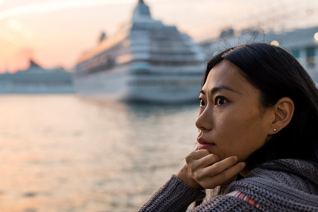 Porträt einer jungen Frau an der Uferpromenade mit Kreuzfahrtschiffen im Hafen im Hintergrund, Kowloon; Hongkong, China.