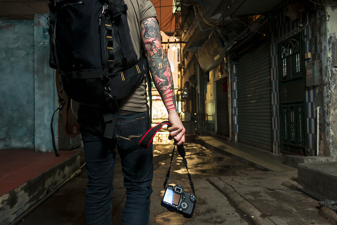 Ein männlicher Reisender trägt seine Kamera durch eine enge Straße; Xiamen, Fujian, China