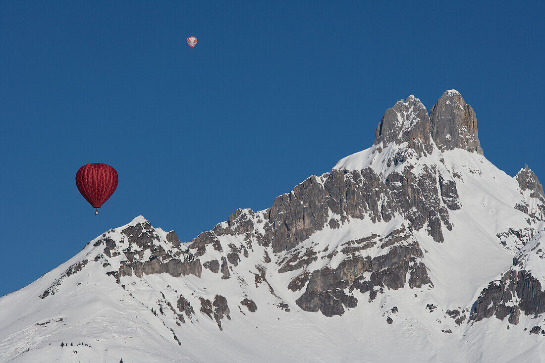 Heißluftballons schweben hoch über den verschneiten Gipfeln der Bischofsmütze während des jährlichen Heißluftballonfestivals des Skigebiets; Filzmoos, Österreich.