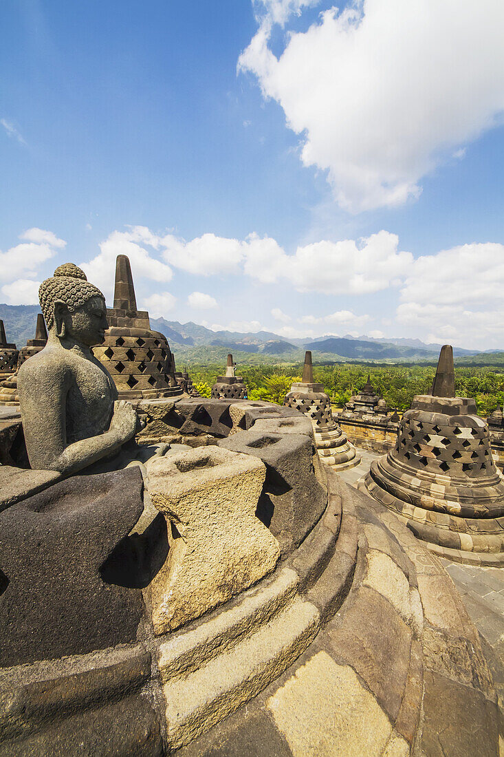 Buddha-Statue mit der Handstellung der Dharmachakra Mudra inmitten der vergitterten Steinstupas mit Buddha-Statuen auf der oberen Terrasse, Borobudur-Tempelanlage, Zentral-Java, Indonesien