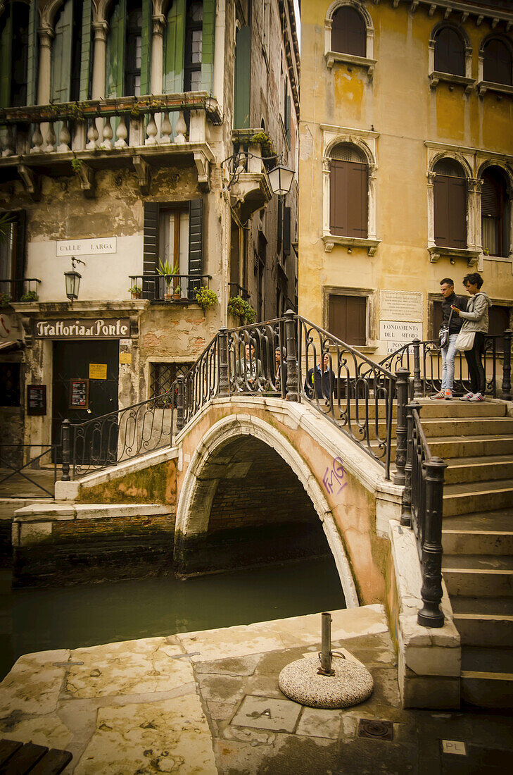 Ein Paar nimmt sich einen Moment auf einer Brücke mit Blick auf den Kanal; Venedig, Italien