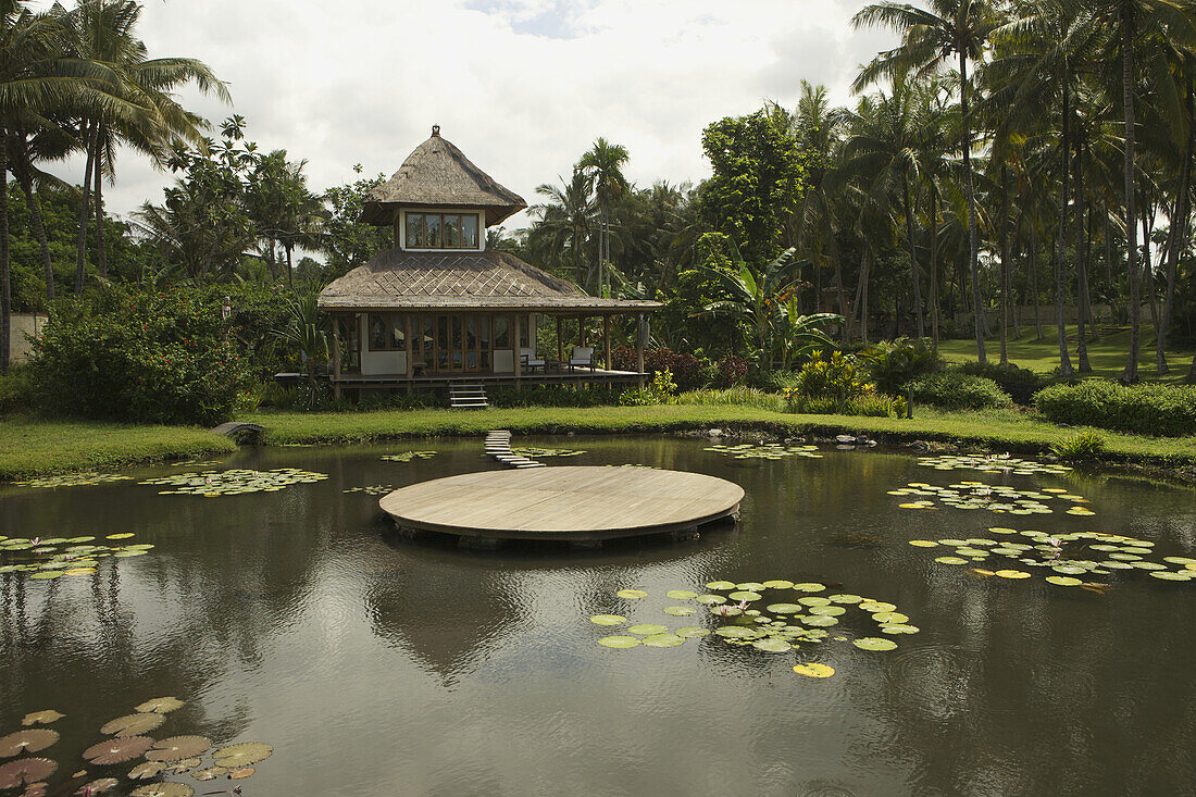 A Small House With Thatched Roof And Pond With Deck; Denpasar, Bali, Indonesia