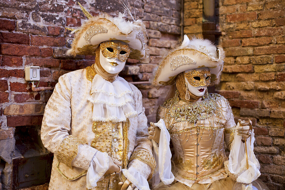 A Man And Woman Dressed In Gold And White Costumes And Masks; Venice, Italy