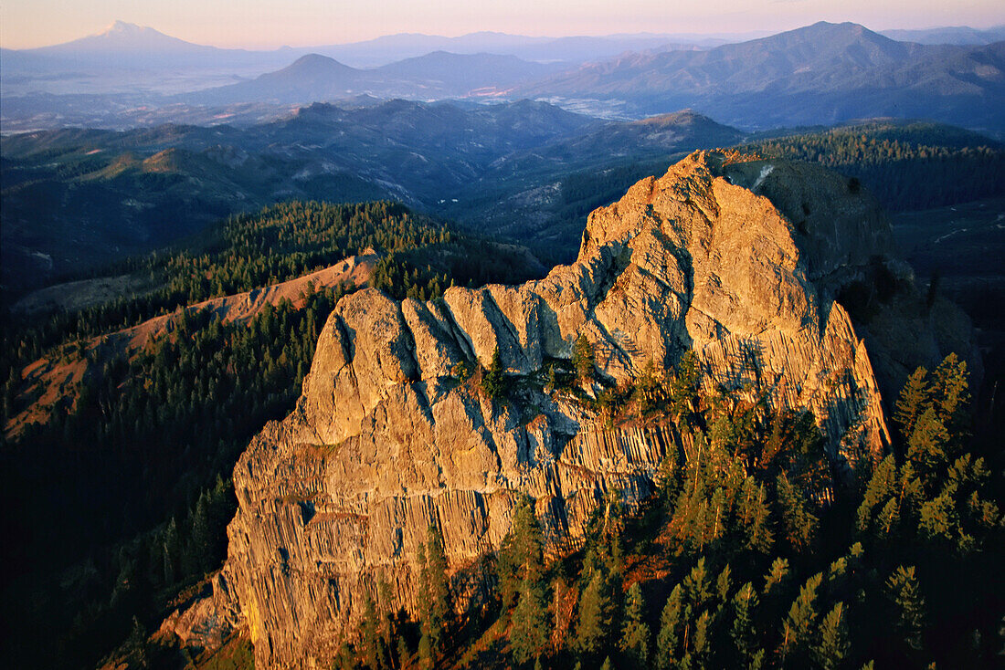 Luftaufnahme des Pilot Rock in der Dämmerung. Die ikonische Felswand ist ein Pfropfen aus vulkanischem Basalt, der 400 Fuß über dem CascadeESiskiyou National Monument an einer Kreuzung von Gebirgszügen, geologischen Epochen und Lebensräumen herausragt. Das 65.000 Hektar große Monument liegt an der Kreuzung der Oregon Cascades und der Siskiyou Mountains mit dem Berg Shasta auf der linken Seite, der sich in der Ferne über die Staatsgrenze in Kalifornien erhebt; Oregon, Vereinigte Staaten von Amerika