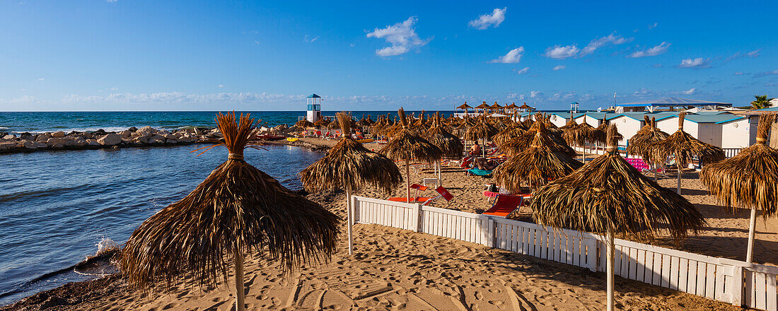 Tiki umbrellas, beach huts and sun loungers on Lido Paradiso Beach near Trapani City; Trapani, Sicily, Italy