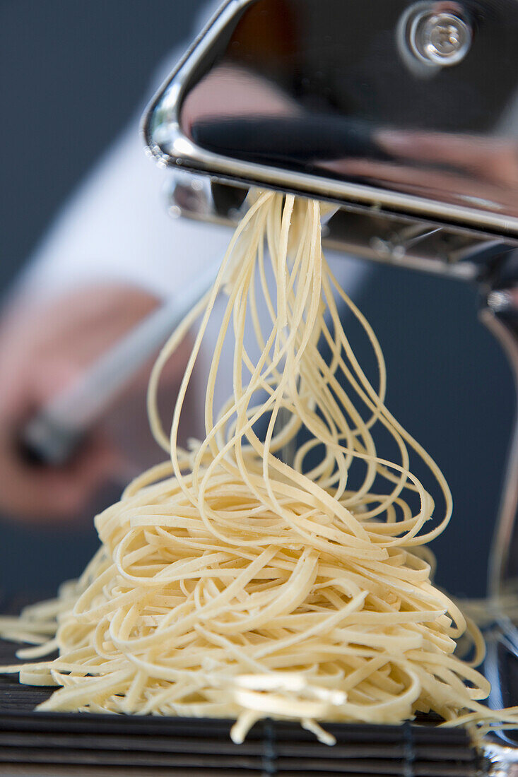 Haufen frischer Tagliolini, die aus einer Nudelmaschine kommen, wobei die Hand den Griff dreht